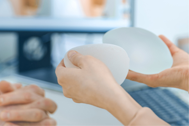 אישה מחזיקה בידה שתלים המשמשים לניתוח הגדלת חזה